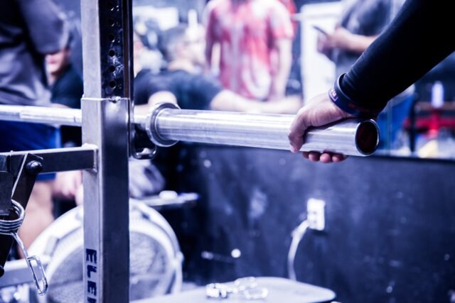A hand sliding a weight onto a barbell, the gym behind it thrown out of focus.