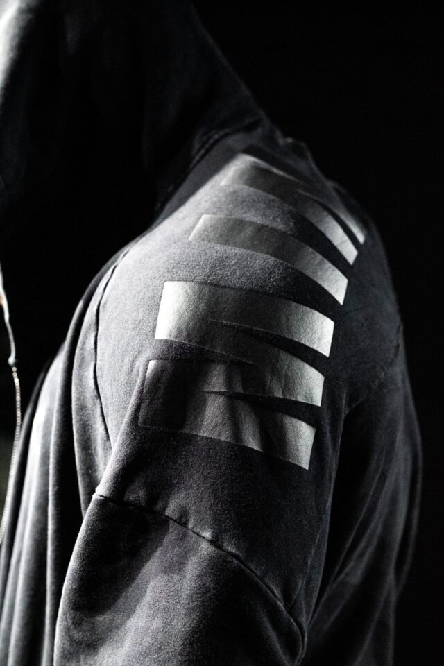 The shoulder of a dark hooded top, lit so that three reflective bands are almost the only thing visible.