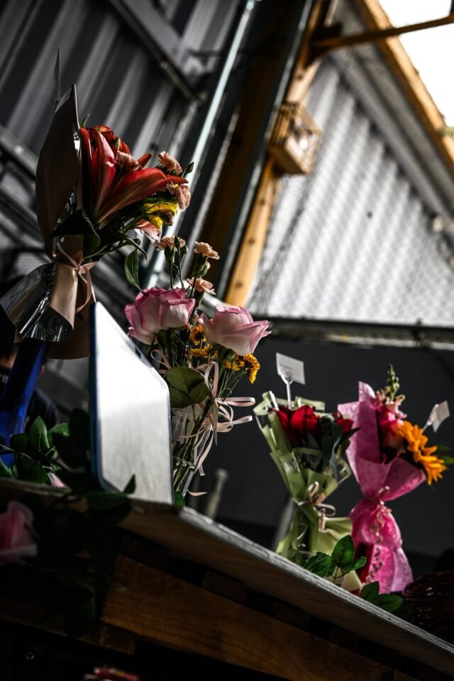 Wrapped bouquets standing by a window beneath a corrugated metal roof.