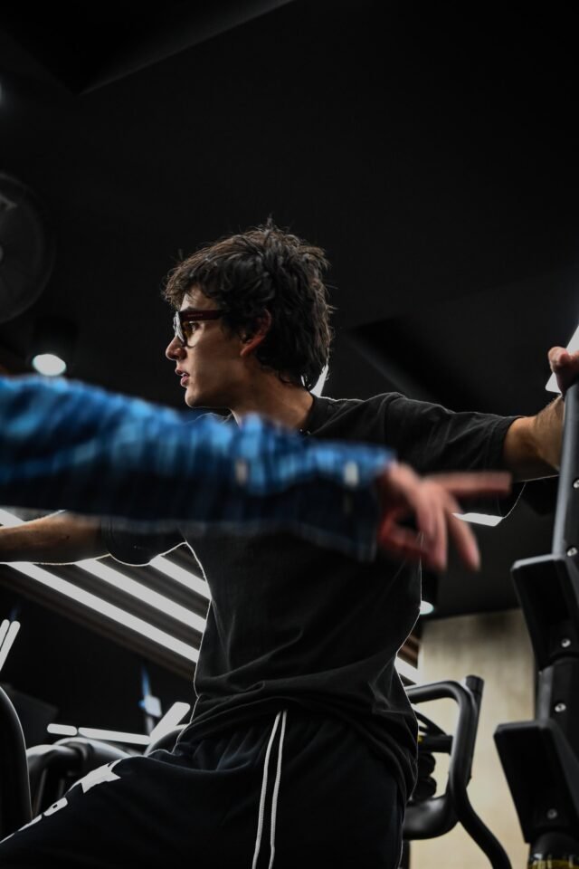 A seated figure in a dark gym, a band of blue light drawn across the frame by a long exposure.