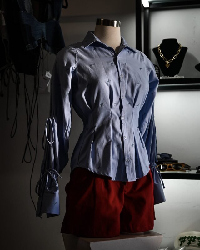 A pale blue shirt pinned on a dressmaker's stand over a red skirt, with garments and jewellery hanging behind it.