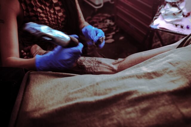 Two gloved hands working close over a forearm resting on a bed.
