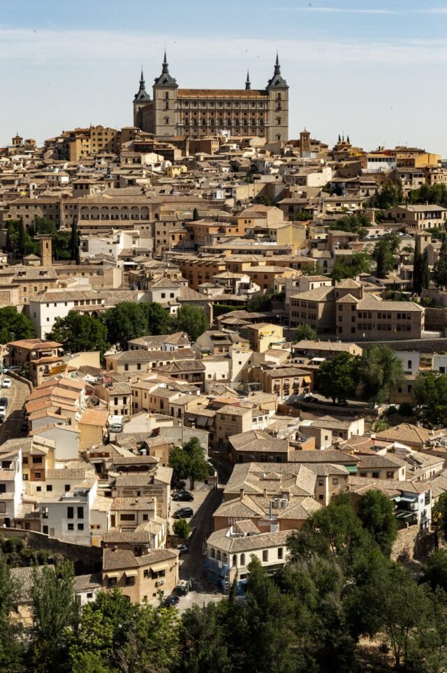 A hillside old town of tiled roofs packed below a square stone fortress with four corner spires.