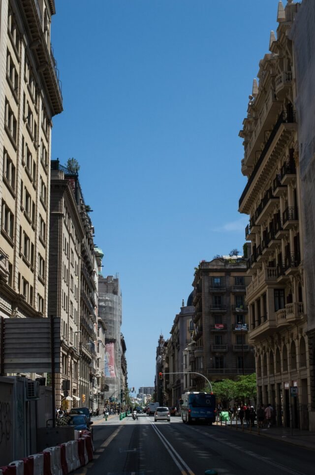 A wide avenue running between tall stone buildings towards a deep blue sky.
